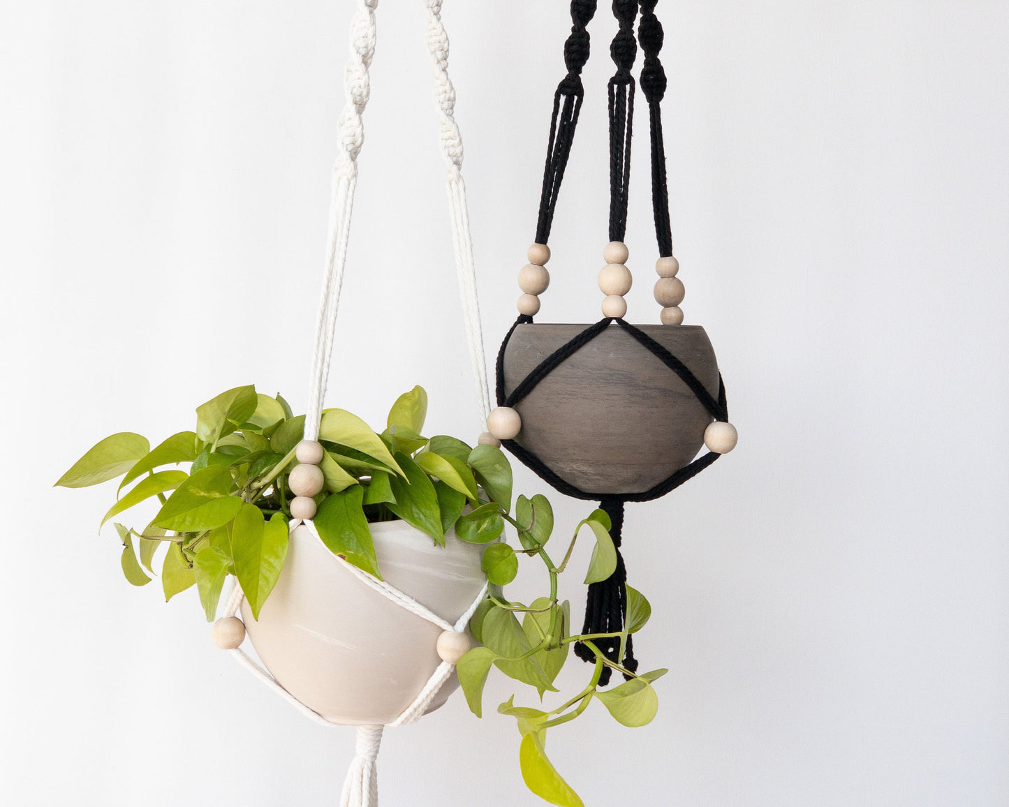 Two macrame plant hangers. One is white, one is black. Each have 3 spiral straps to hold the pots. Each strap has 3 moveable beads that sit just above the pot. Another moveable bead sits at the center of the pot. They have tassels at the bottom.