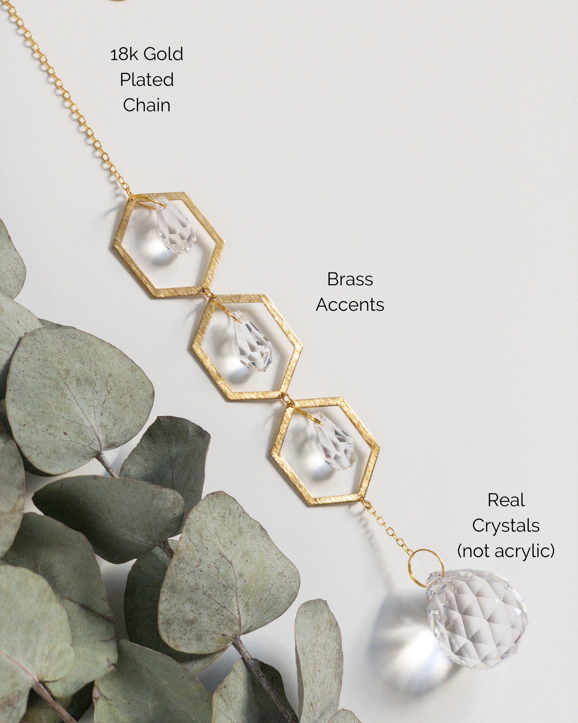 A closeup showing the materials used to make the Brass and crystal suncatcher. Three brass hexagons connected vertically with a small teardrop shaped crystal inside each hexagon. A larger round crystal ball hangs below the bottom hexagon.