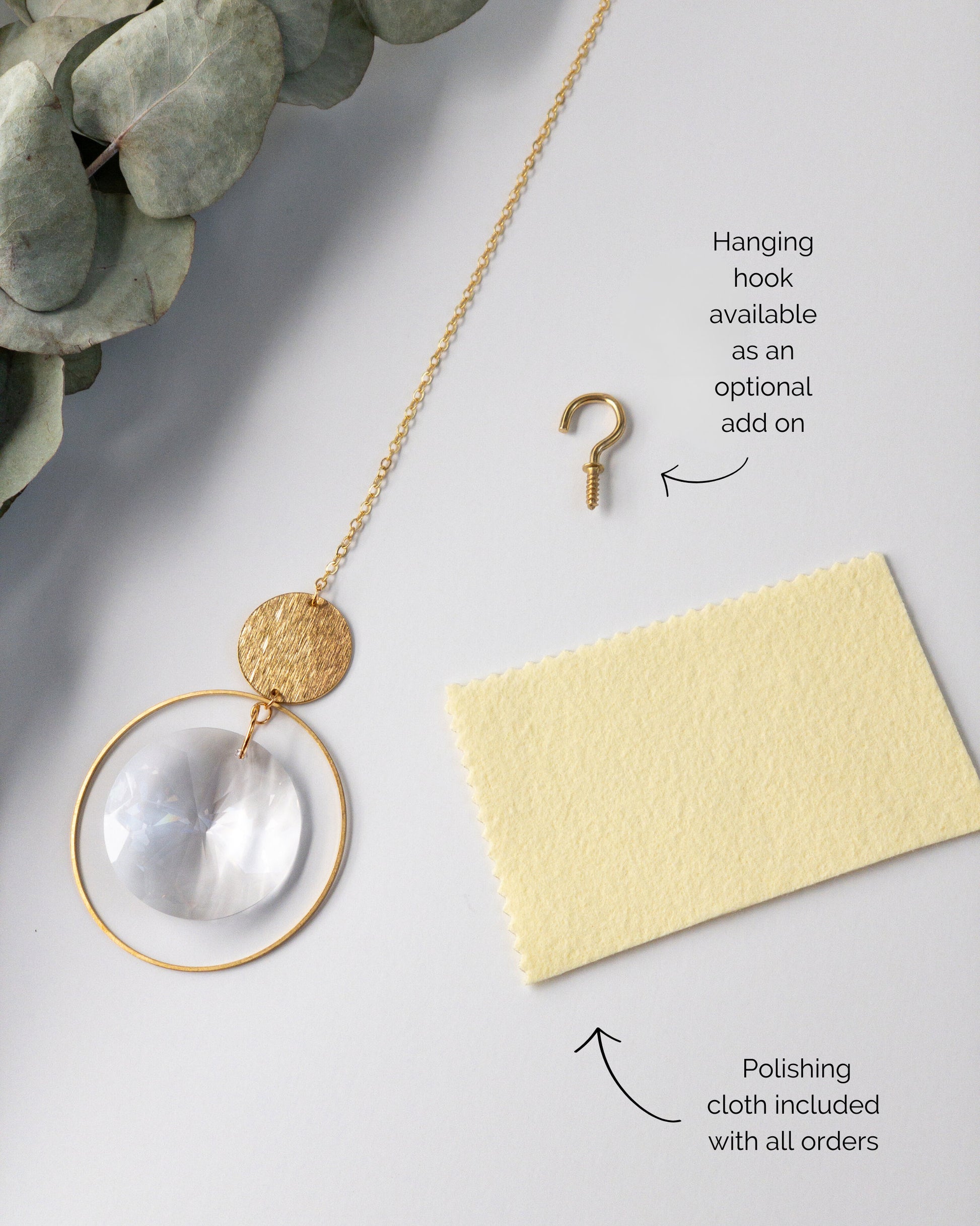Brass and crystal suncatcher that disperses rainbow flecks around the walls and floor. A yellow metal polishing cloth which is included is shown. Also shown is a small brass hook which can be used to hang the sun catcher.